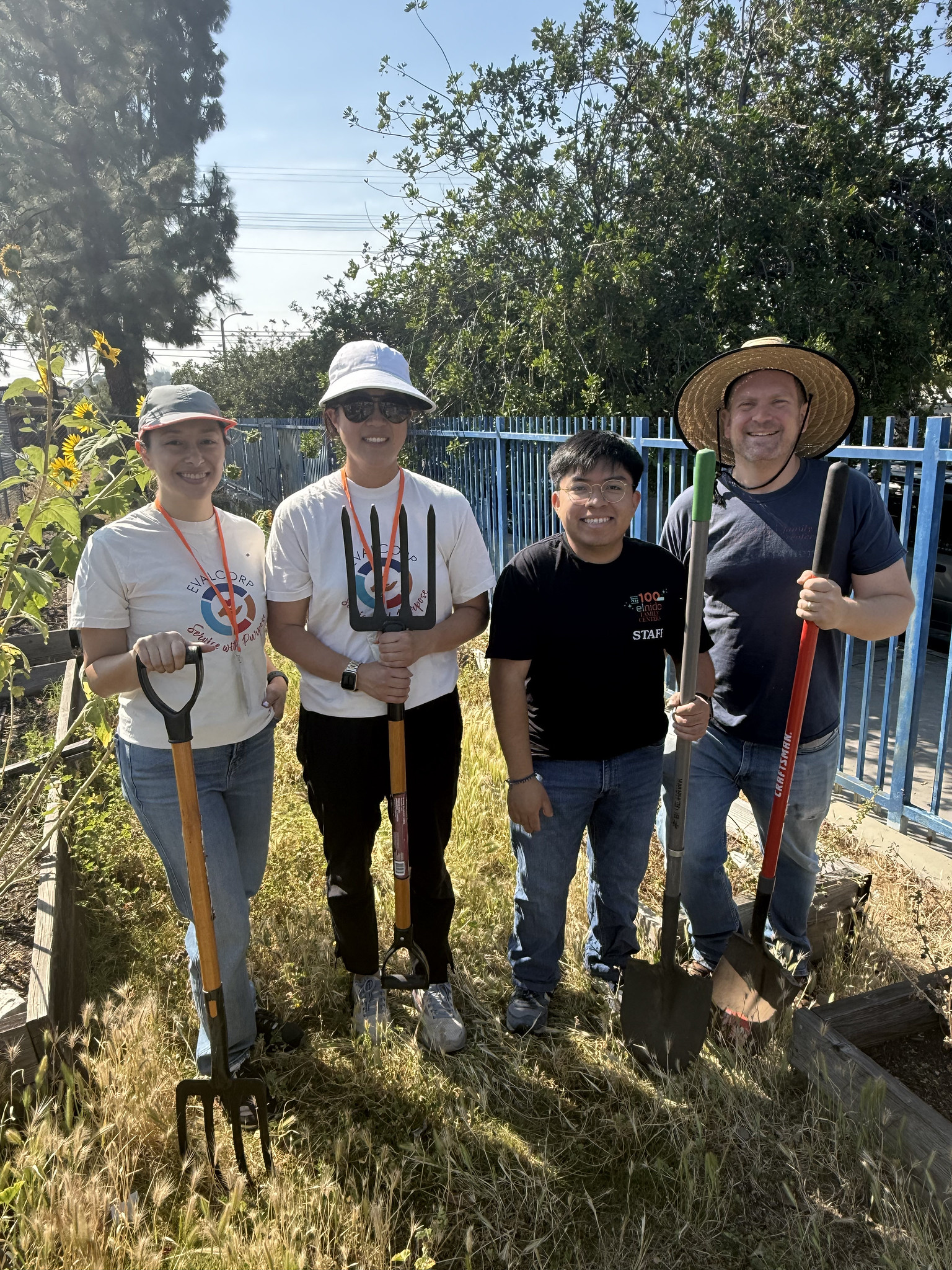 Photo of team members Alex and Celina with gardening tools posing with members of El Nido staff at community garden