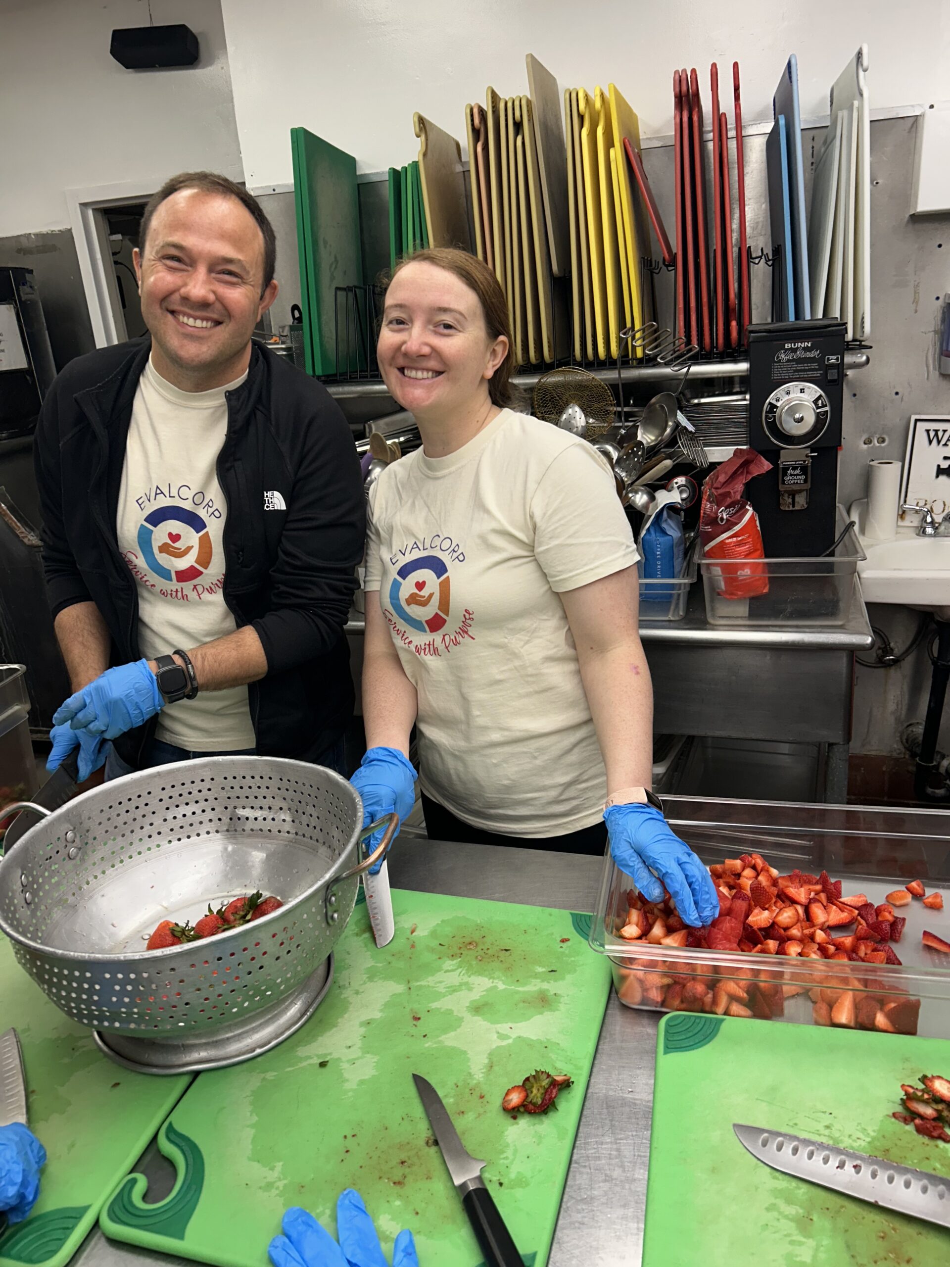Photo of team members Luis and Shayla volunteering in soup kitchen by chopping strawberries
